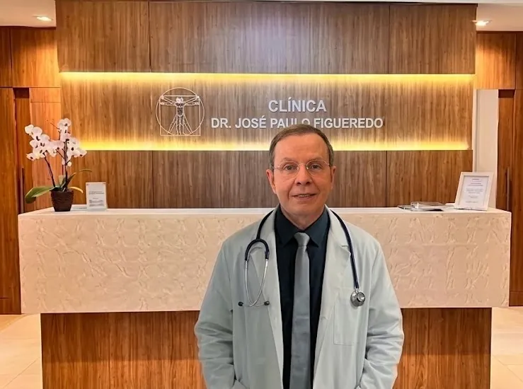 Dr. José Paulo Figueredo em frente à recepção da clínica, junto ao logotipo do Homem Vitruviano